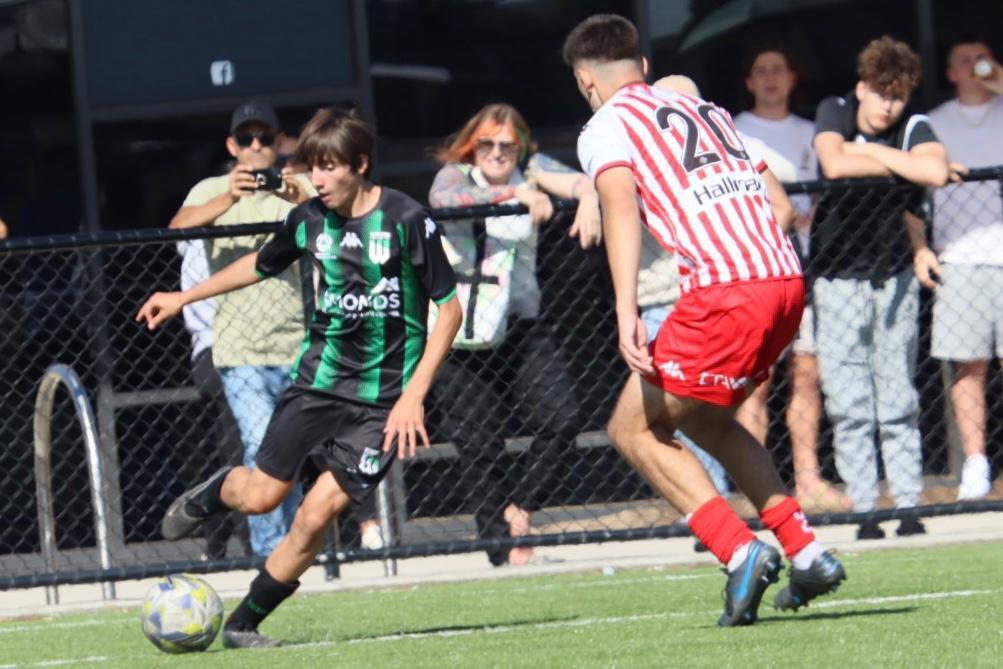 Players in a competitive football match under a coach's observation